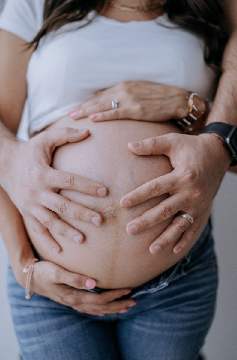 Cuatro manos sosteniéndose sobre la panza de la mamá embarazada