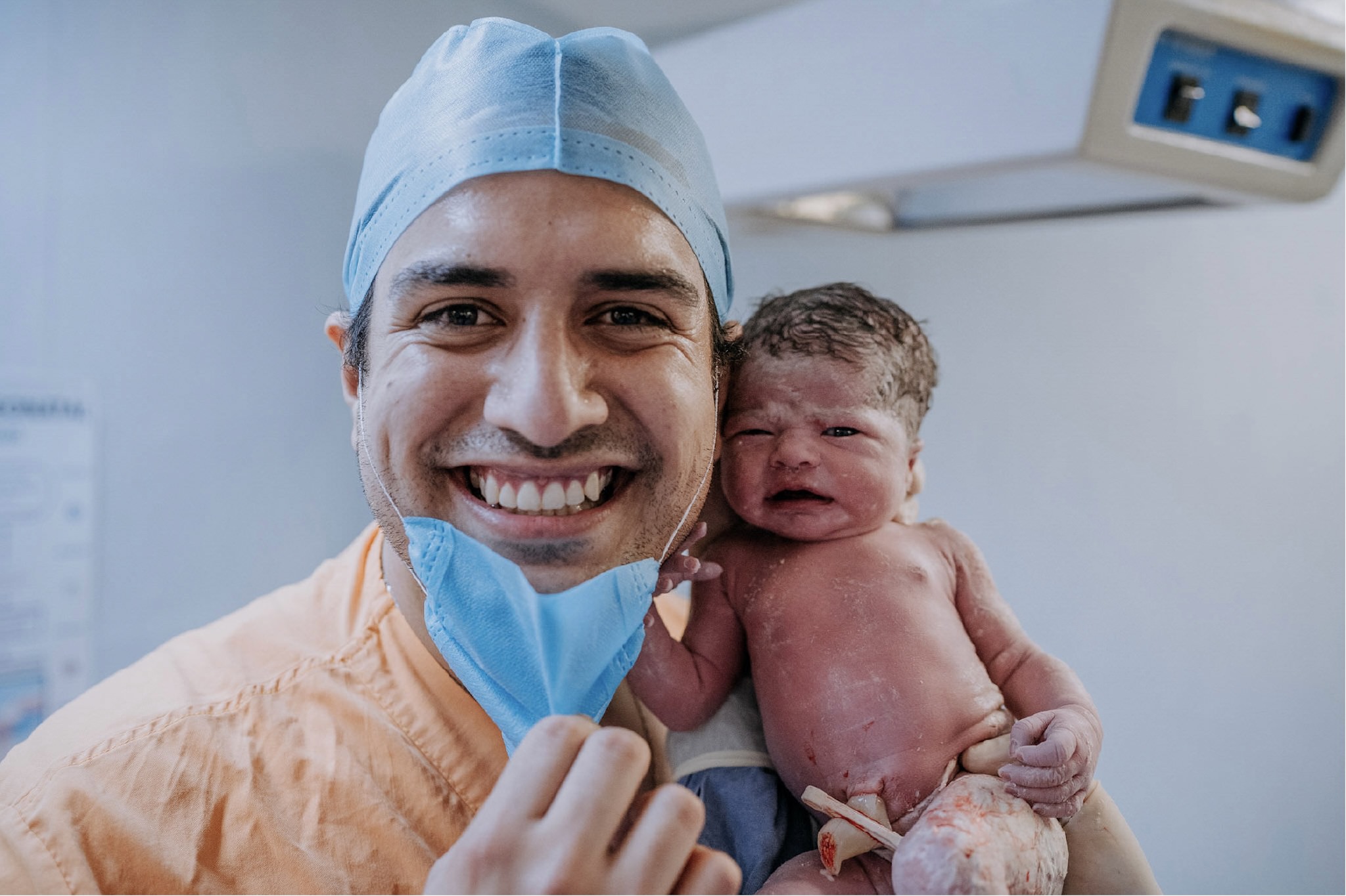 Papá sonriendo con el cubrebocas bajado, sosteniendo a su bebé recién nacido junto a su mejilla